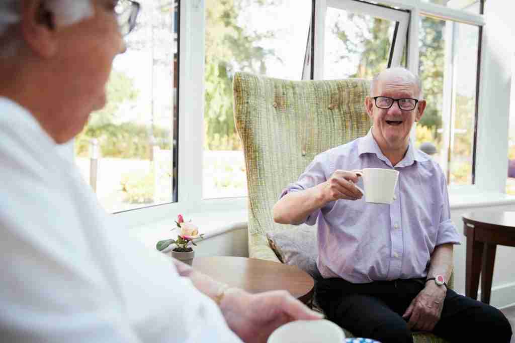 Male And Female Residents Sitting In Chairs and Talking In Retirement Home