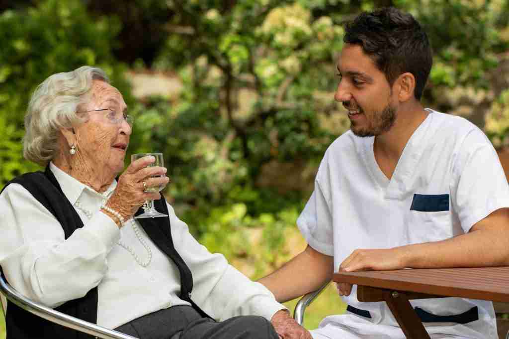 Senior woman sitting in garden next to male assistant.