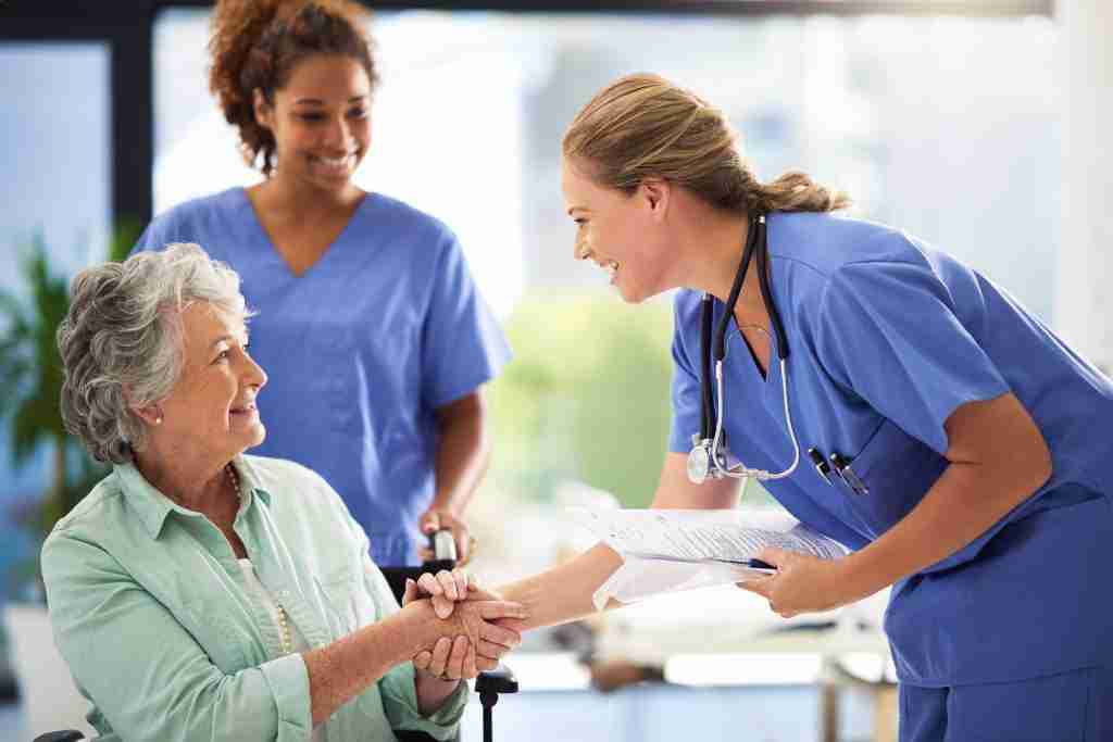 Handshake, nurse smile and senior woman in wheelchair with medical results and surgery success news. Hospital, healthcare and clinic with women and nursing staff with care and help of elderly person.
