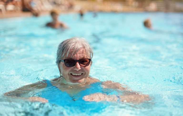 Elderly senior woman with grey hair, wearing blue swimsuit smiling in hotel pool